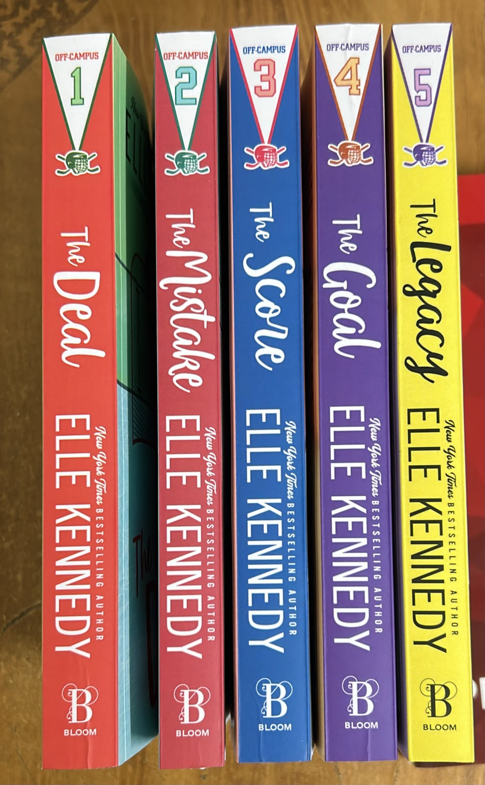 Five hardcover books from The Cleopatra Chronicles series by Elle Kennedy, standing upright in a row. The spines are colored red, pink, blue, purple, and yellow, with white text and numbers 1 through 5.